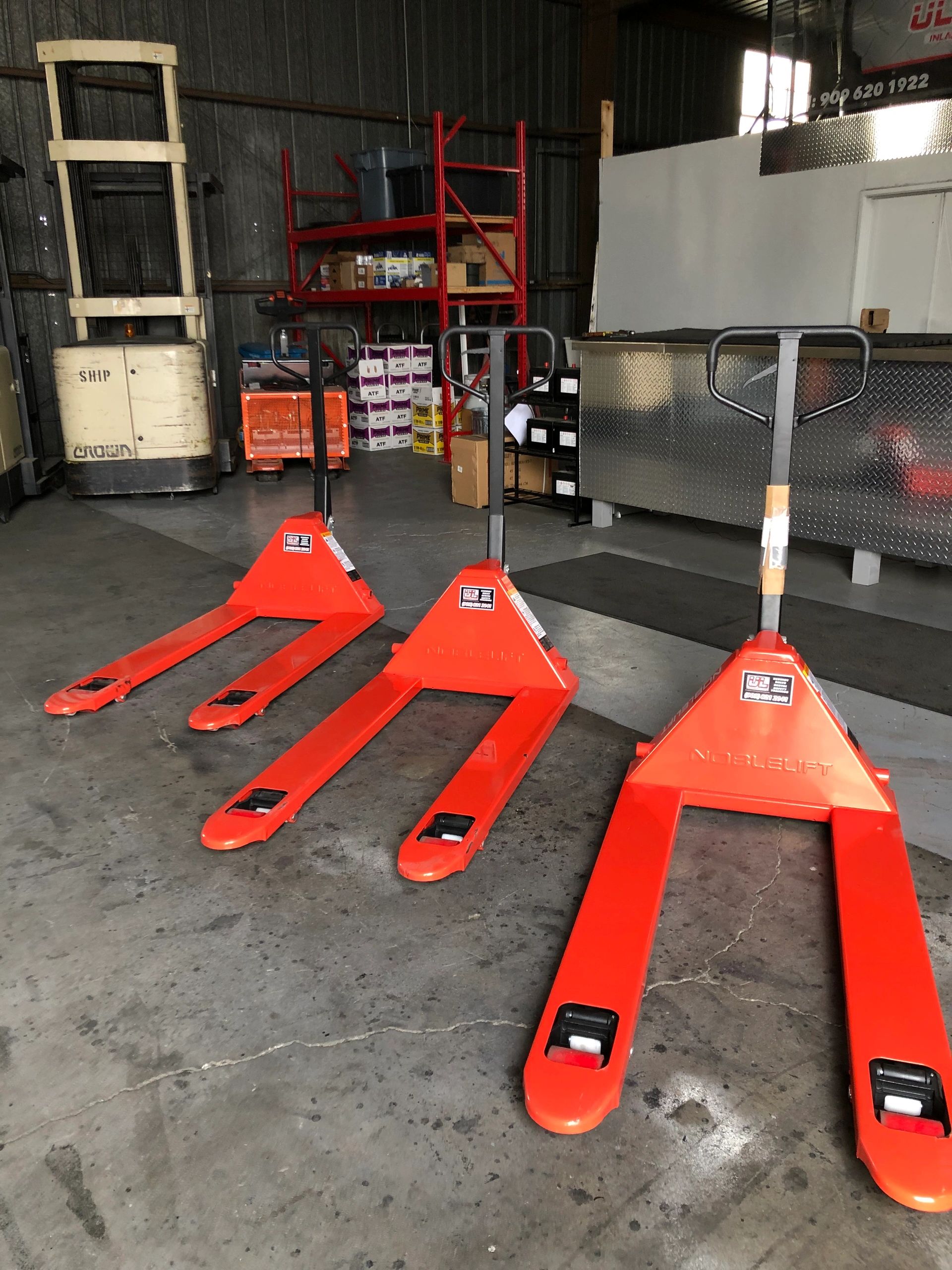 Brand-new orange pallet jacks lined up in the Ultimate Lift warehouse.